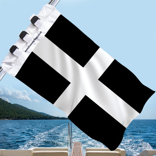 Cornwall county flag with a bold white cross on a black background, mounted on a boat rail with a universal triple-lock system, flying at sea with blue sky and coastline in the background