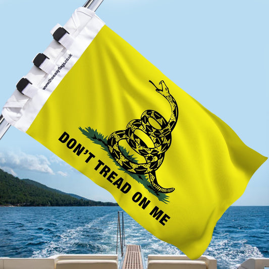 Don’t Tread on Me” Gadsden flag with rattlesnake design, mounted on a boat rail with a universal triple-lock system, flying at sea with blue sky and coastline in the background