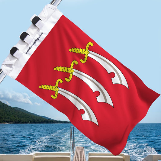 Essex county flag with red background and three white seaxes (swords), mounted on a boat rail with a universal triple-lock system, flying at sea with blue sky and coastline in the background