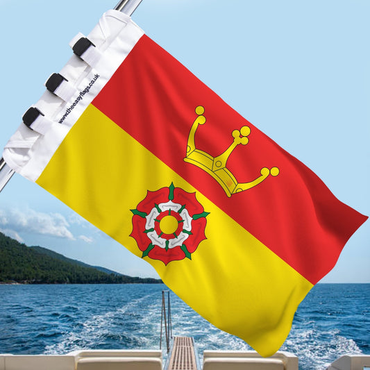 Hampshire county flag with red background, gold castle and Tudor rose, mounted on a boat rail with a universal triple-lock system, flying at sea with blue sky and coastline in the background
