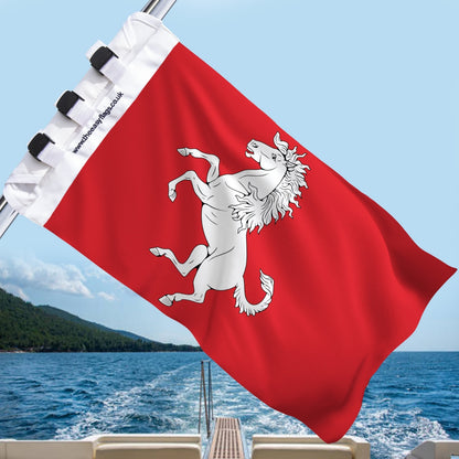 ent county flag with red background and white horse rampant (Invicta Horse), mounted on a boat rail with a universal triple-lock system, flying at sea with blue sky and coastline in the background