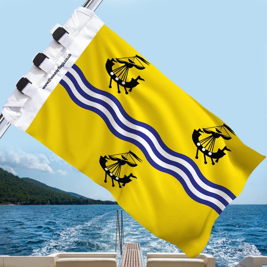Outer Hebrides (Western Isles) county flag with golden background, vertical blue and white wavy stripes, and four black ships, mounted on a boat rail with a universal triple-lock system, flying at sea with blue sky and coastline in the background