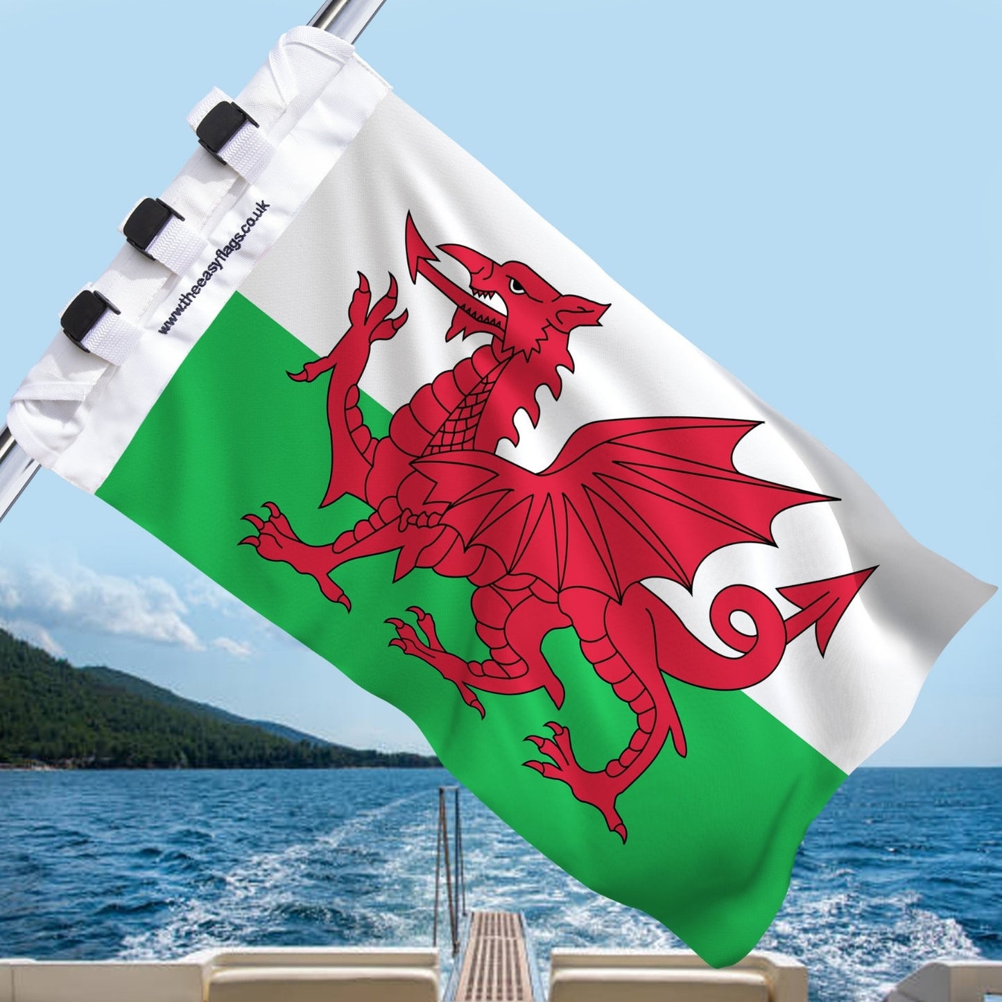 Wales national flag with red dragon on green and white background, mounted on a boat rail with a universal triple-lock system, flying at sea with blue sky and coastline in the background