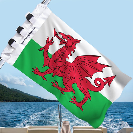 Wales national flag with red dragon on green and white background, mounted on a boat rail with a universal triple-lock system, flying at sea with blue sky and coastline in the background